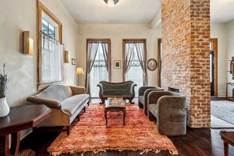 Expansive living room featuring vintage seating, tall windows, and an original exposed-brick chimney as the centerpiece.