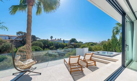 A sunny terrace with lounge chairs, a hanging chair, and a jacuzzi offers a relaxing outdoor space with a scenic view.