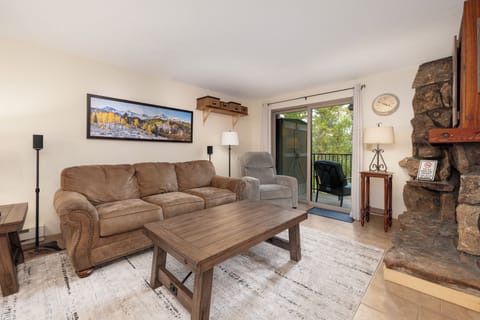 Cozy up in this warm living room featuring a stone fireplace, comfortable seating, and peaceful views through your private balcony.