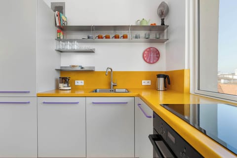 Another angle of the yellow-accented kitchen, featuring open shelves and a window view. The layout maximizes space.