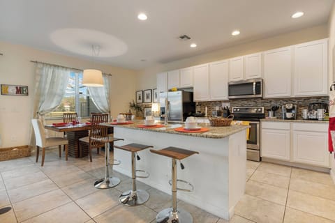 This bright kitchen boasts sleek white cabinetry and a spacious island perfect for casual dining. Natural light fills the space, accentuating the stylish bar stools and warm tile flooring for an inviting cooking atmosphere.