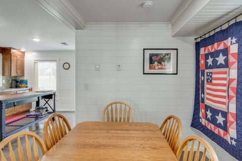 Dining area | Wooden table with chairs, white shiplap walls, quilt wall hanging, and view into the kitchen