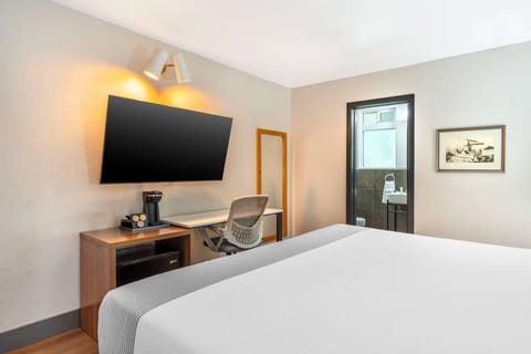 Work desk with TV, coffee maker, and chair beside cozy bed