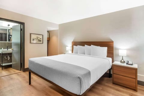 King bed with soft white linens and lamps near the bathroom door