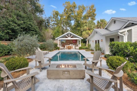 Elegant backyard oasis featuring swimming pool, fire pit seating area, and charming poolside pavilion surrounded by lush landscaping.