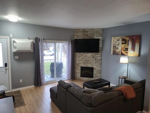 Bright open living room with modern stone fireplace, comfy sectional sofa, smart TV, and direct access to the front balcony