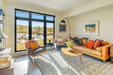 Relax in your stylish living space with vibrant orange leather sofa, modern décor, and stunning city views through floor-to-ceiling windows.