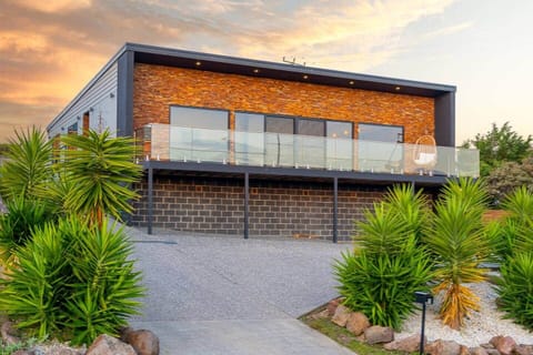 Modern hillside retreat with stunning glass-panel balcony, stone façade, and lush greenery. Enjoy captivating sunsets and a serene atmosphere, perfect for families or groups seeking a luxurious getaway close to nature and urban convenience.