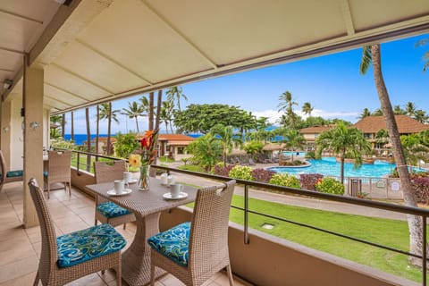 Ocean-view lanai with cushioned seating, perfect for relaxing while overlooking lush gardens and sparkling blue waters.