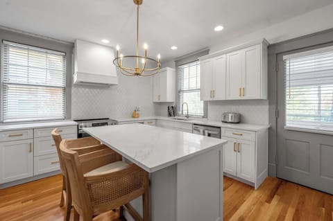 This luminous and refined culinary space boasts marble-style counters, striking hardware, and a comfortable island perfect for casual dining.