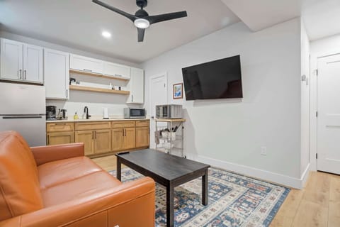 This angle shows how the living room connects seamlessly to the kitchenette, giving the space an open, functional layout. The leather seating, Smart TV, and warm wood cabinetry create a clean, modern look throughout.