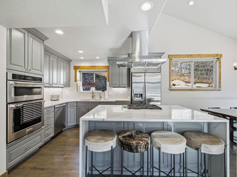 Modern chef's kitchen featuring sleek grey cabinetry, stainless steel double ovens, and a massive quartz island under soaring vaulted ceilings.