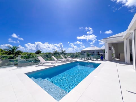 Modern turquoise pool surrounded by sun loungers and a bright terrace, offering a clear view over tropical greenery.