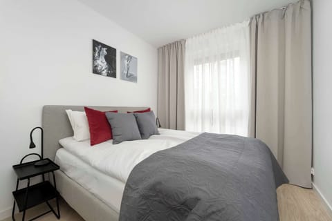Bright bedroom with a double bed, grey bedding, and large curtains letting in natural light.