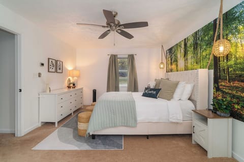 Spacious primary bedroom with Woodland Sunrise feature wall, queen bed, plush linens, and peaceful forest views.