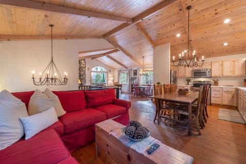 Cozy up in your mountain retreat where rustic wood beams frame an inviting open-concept space. Sink into the plush red sectional sofa and feel the warmth of home as natural light streams through windows.
