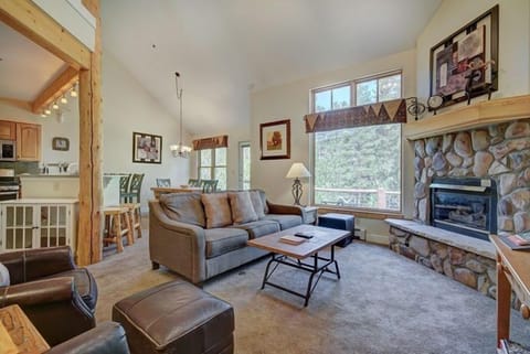 Bathed in natural light, the inviting living space beckons with its cozy furnishings and the warmth of a stone fireplace—a perfect retreat after a day on the slopes.