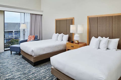 Two double beds with soft lighting and chair by large window