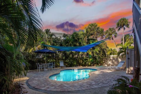 Stunning tropical sunset paints the sky as palm trees frame this private pool oasis with shade sail and outdoor dining.