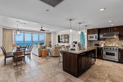Open kitchen and dining space featuring a central island with granite surface, pendant lights, and panoramic views of turquoise waters.