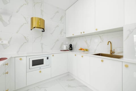 A white marble kitchen with golden fixtures and modern cabinetry. The combination of marble patterns and metallic accents feels luxurious. The workspace appears bright and functional.