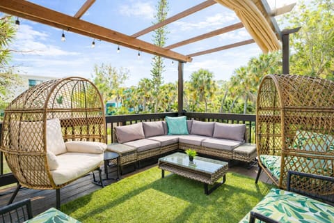 Breezy pergola lounge with sectional sofa, two wicker egg chairs, string lights, and sweeping tropical treetop views.