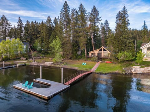 Lakefront A-frame cabin with private dock, Adirondack chairs, and pine-forest backdrop — the shot guests screenshot before they book