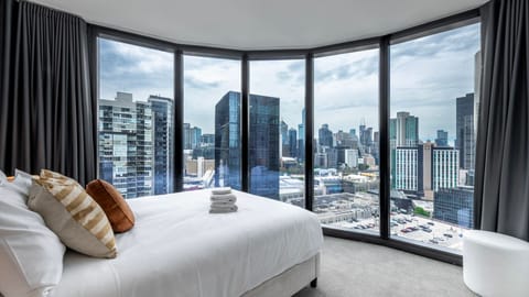 Bright bedroom with panoramic floor-to-ceiling city views.