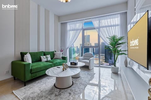 Step into a bright, stylish living area with a plush green sofa, marble coffee tables, and a 65” Smart TV. Floor-to-ceiling windows open to skyline views, filling the space with natural light and Downtown Dubai charm.