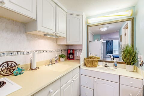 Charming beach stay kitchenette with bright white cabinets, handy cooktop, and adjoining vanity area. A cozy, efficient setup perfect for prepping meals and refreshing after a day by the ocean.