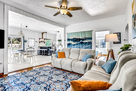Relax in this open-concept beach stay living room, featuring comfy sofas, vibrant coastal décor, and easy flow to the dining and kitchen areas—perfect for unwinding after a day by the ocean.