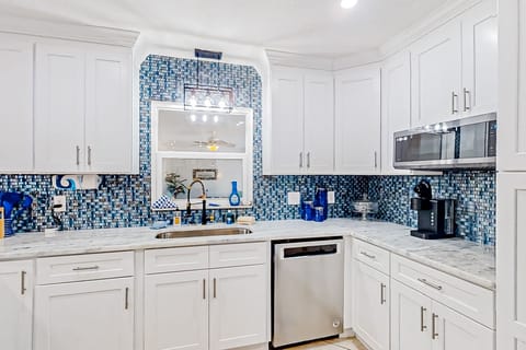 This fresh, beach-inspired kitchen features marble counters, sleek appliances, and a vibrant blue backsplash—an inviting space to cook and gather during your beach stay.