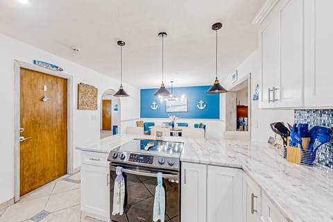 This bright, beach-inspired kitchen flows into a nautical dining area, featuring marble counters and stylish lighting—an inviting space to cook, gather, and enjoy your beach stay.