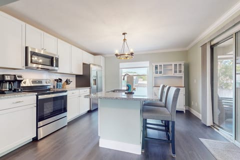 This bright, beach-inspired kitchen features stainless appliances, a spacious island, and plenty of natural light—perfect for cooking, gathering, and enjoying your beach stay.