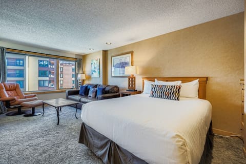Relax in your spacious suite with a comfortable queen bed, cozy seating area, and large windows offering city views for a perfect retreat.