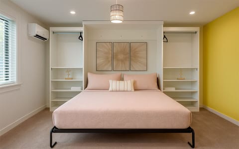 Wide view of The Gold Room at Garden of Manors, showing the bright bedroom, storage, mini-fridge, and sunny accent wall in Wilton Manors.
