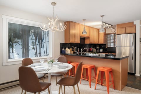 Your stylish open kitchen features modern appliances and breakfast bar, perfect for preparing meals while enjoying snowy forest views through the large window.