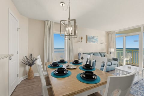 Bright dining area with seating for six, surrounded by floor-to-ceiling windows and an end-unit bonus window. Ideal for vacation meals, family game nights, and enjoying coastal views during your North Myrtle Beach getaway.