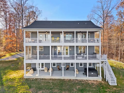 Aerial Rear View - All three levels of covered porches, the hot tub, swing chairs, and green yard leading down to the water.