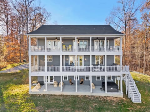 Aerial Rear View - All three levels of covered porches, the hot tub, swing chairs, and green yard leading down to the water.