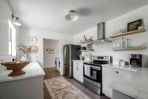 The modern kitchen features a sleek stainless steel side-by-side refrigerator with a bottom freezer, an electric flat top range, floating shelves, and generous countertop space for effortless meal prep.
