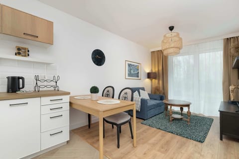 A bright dining and living area featuring a small wooden dining table with chairs and a cozy sofa. Natural light fills the space through large windows.