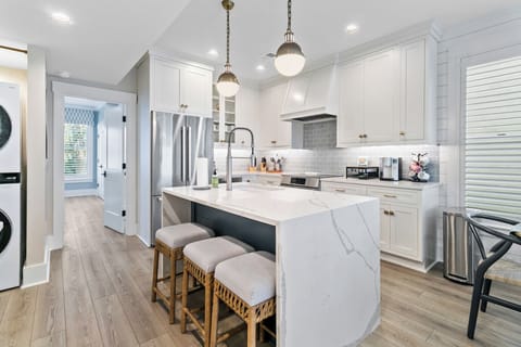 Crisp white cabinetry, warm wood floors, and a sleek waterfall island create a bright, welcoming space designed for both style and everyday comfort.