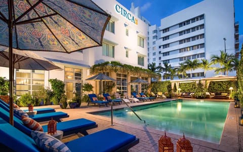 Inviting pool at dusk with lounge chairs, umbrellas, and soft lights