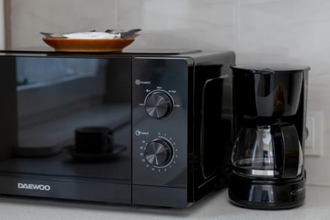 A black microwave and coffee maker positioned together on a kitchen counter against a glossy backsplash.