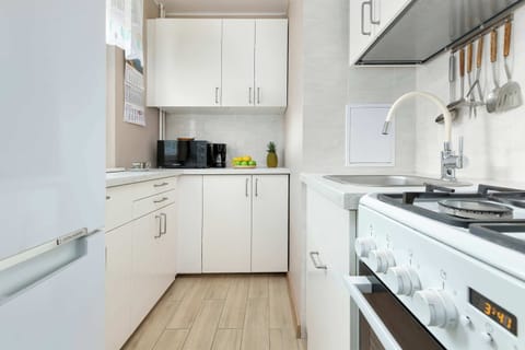A compact white kitchen with modern cabinets, a gas stove, and a wooden floor.