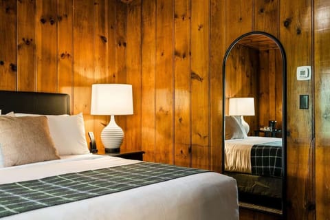 Warm wood-paneled room with bed, lamp, and full-length mirror