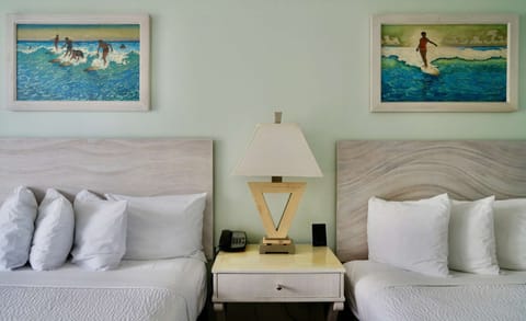 Two beds with beach artwork and lamp on nightstand