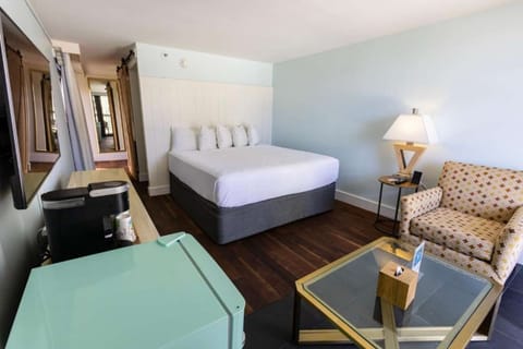 Room with a king bed, armchair, fridge, and coffee maker station