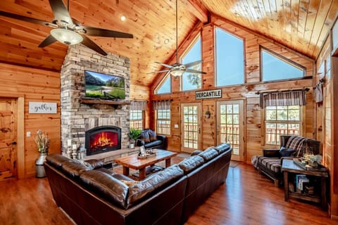Spacious upstairs living room with soaring ceilings, stone fireplace, and large windows overlooking the forest